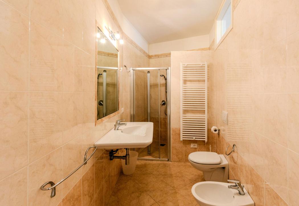 Salle de bain avec douche, lavabo, bidet, toilettes et carrelage beige.