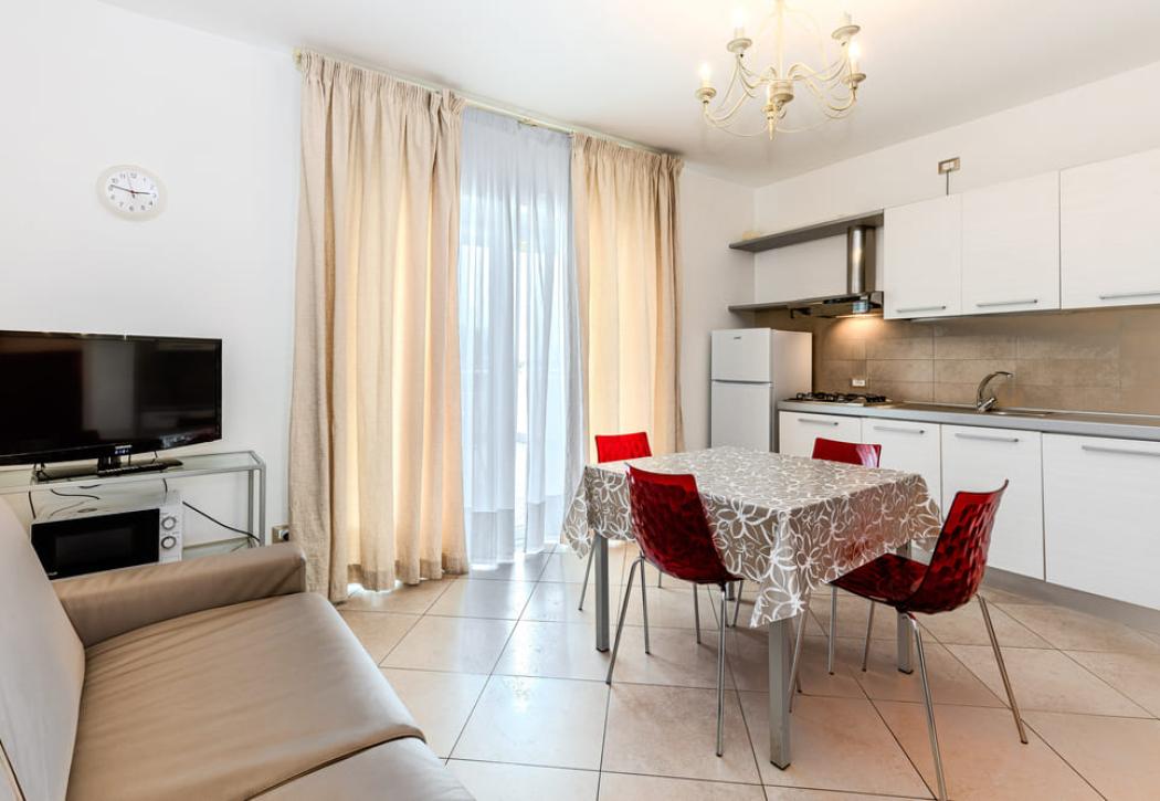 Cuisine moderne avec table, chaises rouges, TV et canapé beige.