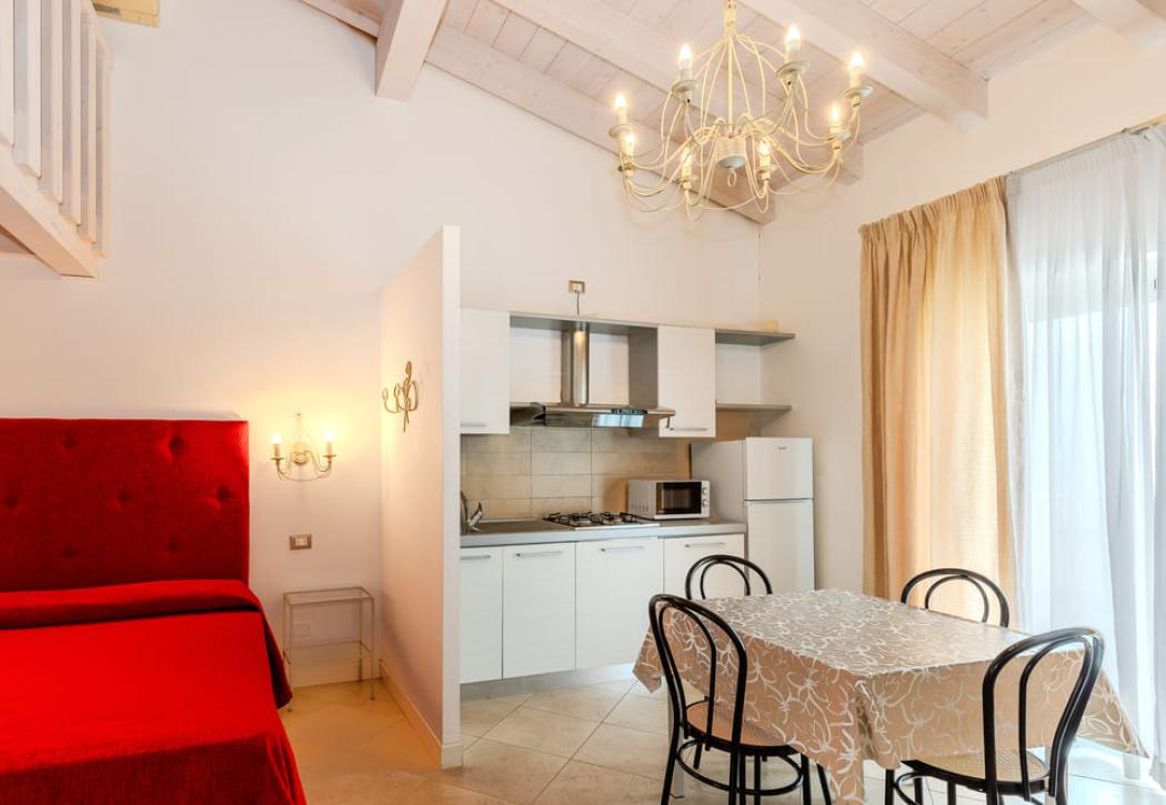 Studio lumineux avec cuisine, lit rouge et table à manger.