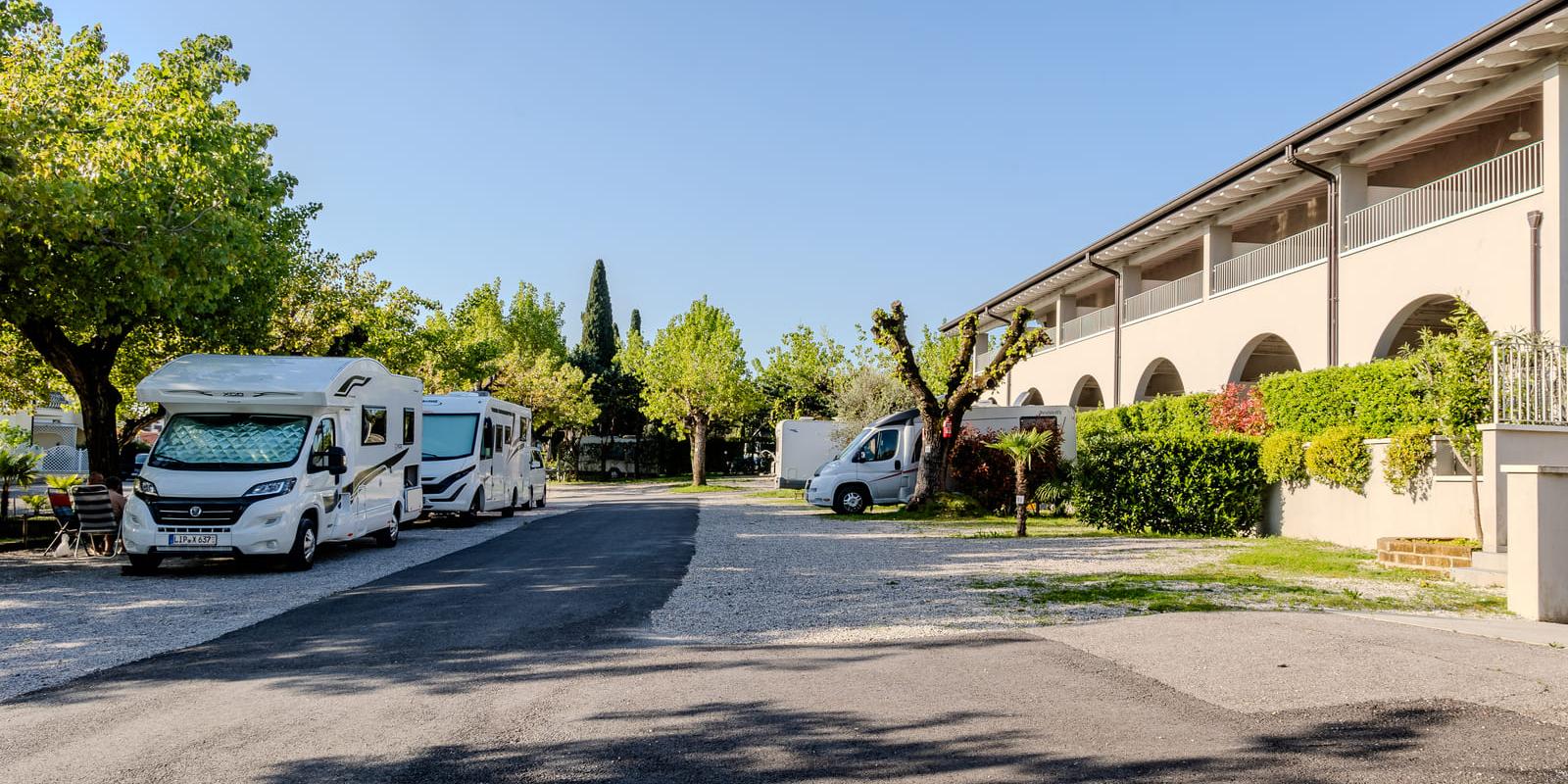 Wohnmobilstellplatz mit Bäumen und Gebäude rechts.