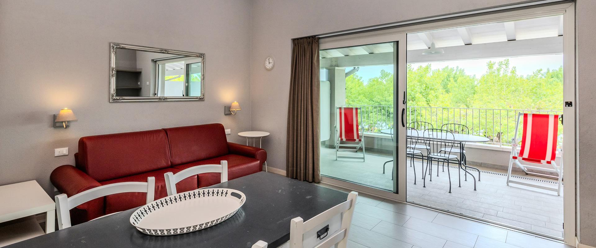 Salon lumineux avec canapé rouge et balcon donnant sur la verdure.