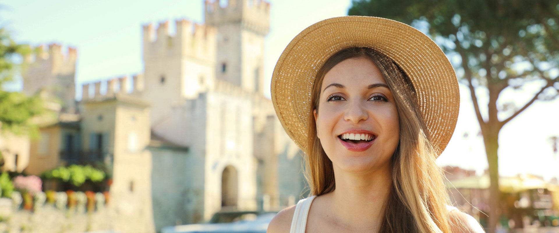 Smiling woman with straw hat in front of a castle.