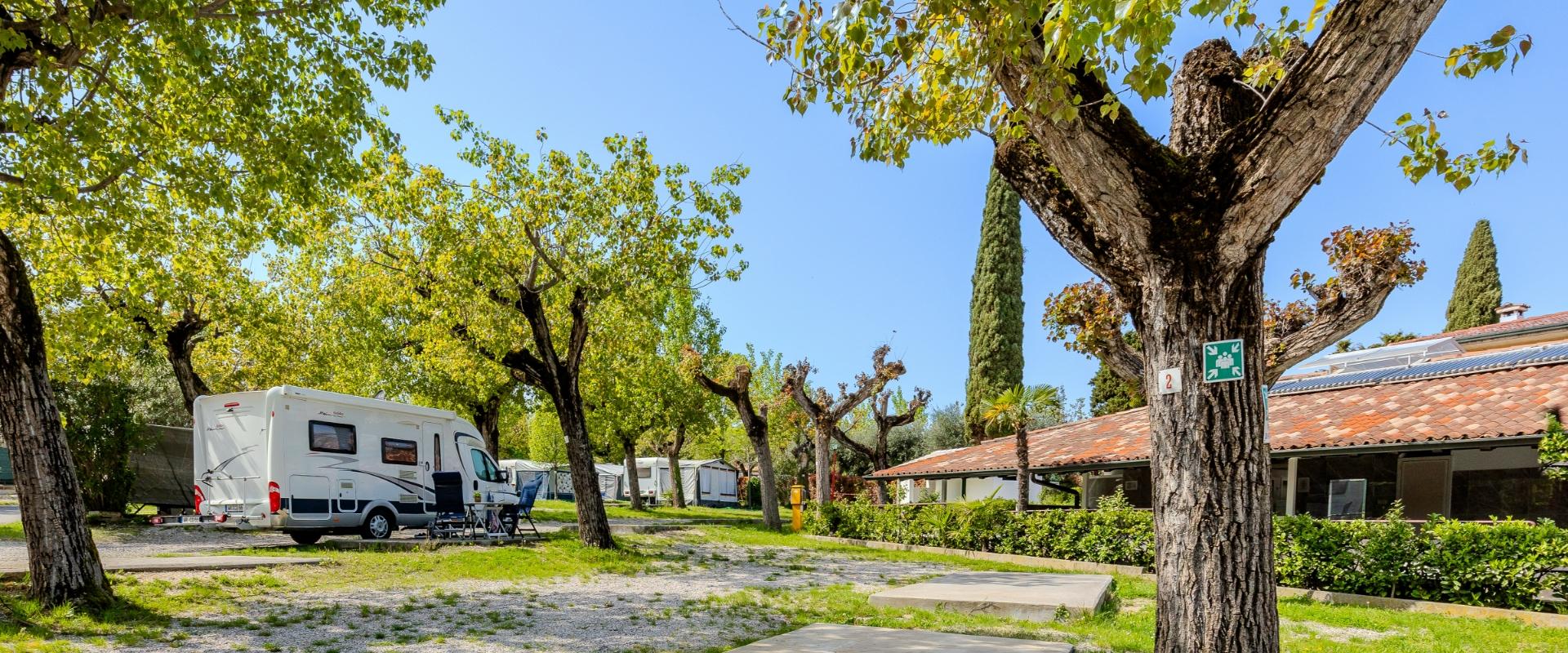 Campingplatz mit Wohnmobil zwischen Bäumen, Picknickbereich und Einrichtungen.