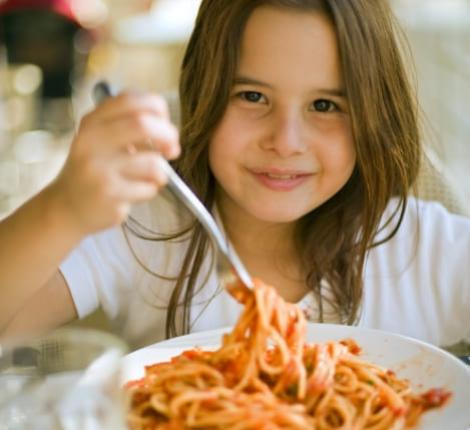 Bambina sorridente mangia spaghetti con salsa di pomodoro.